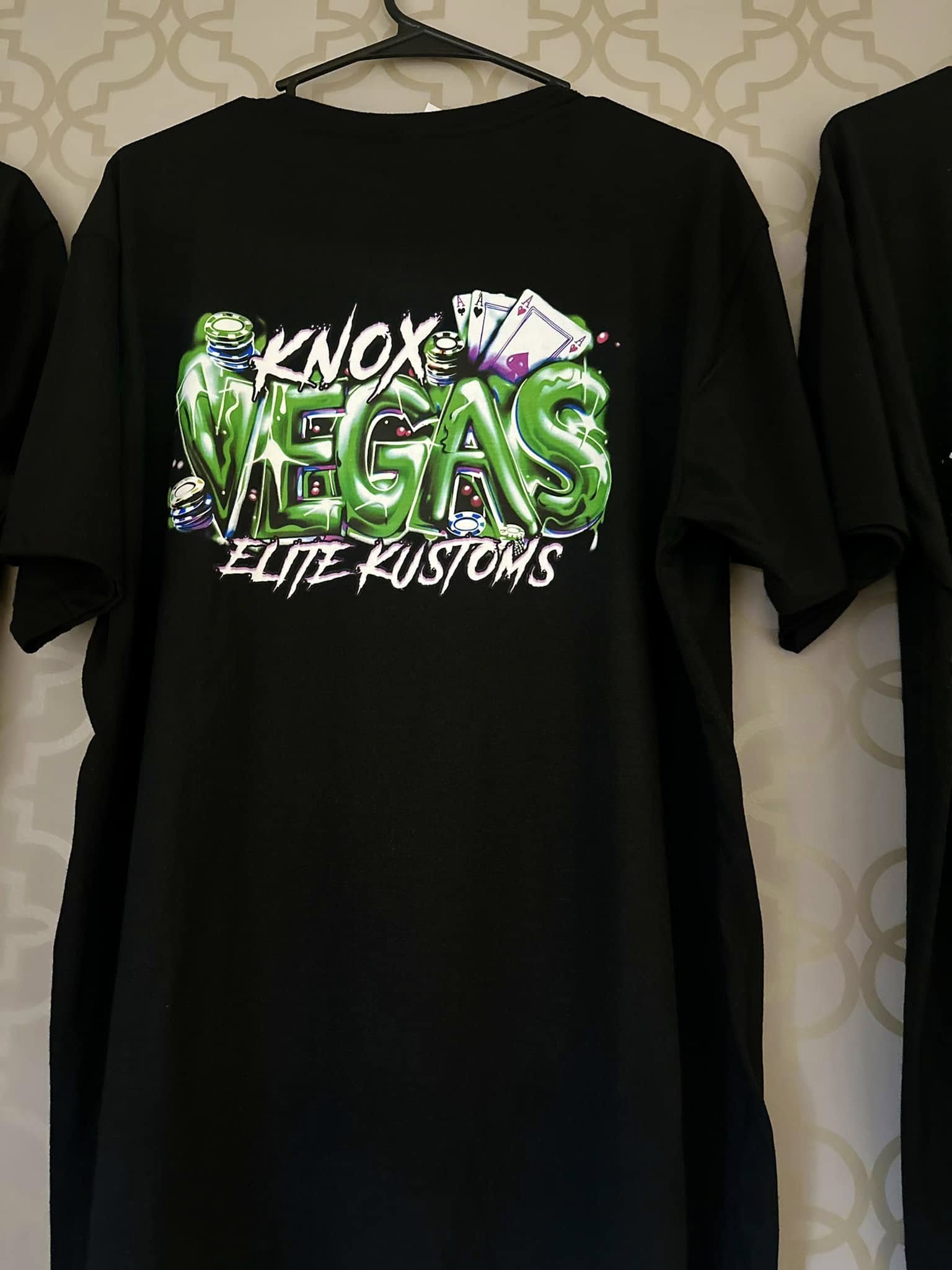 Black t-shirt with 'Knox Vegas Elite Kustoms' graphic design on a patterned wall background